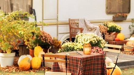 Herbstlich dekorierter Gartentisch mit Stühlen vor einem Wohnwagen.