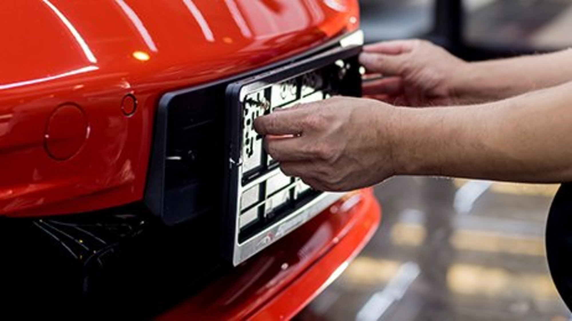 Techniker wechselt das Kennzeichen auf einem roten Auto