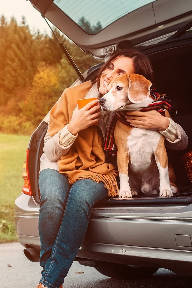 Frau sitzt mit ihrem Hund auf der Kofferraumkante Frau sitzt mit ihrem Hund auf der Kofferraumkante
