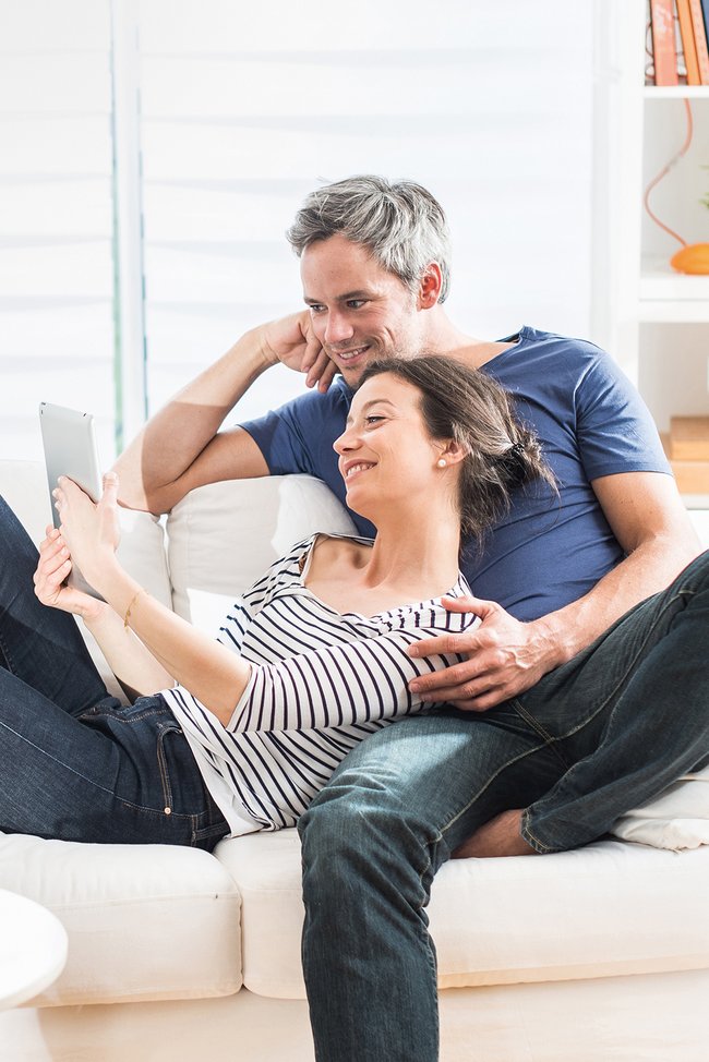 Paar sitzt auf der Couch und sieht auf ein iPad.