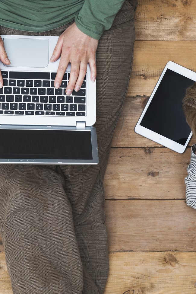 Symbolbild Onlineprodukte. Mutter und Kind sitzen am Boden und arbeiten auf Laptop und Tablet