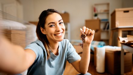2291693015 Junge glückliche Frau macht ein Selfie während Sie den Schlüssel von Ihrem neuen Apartment hochhält