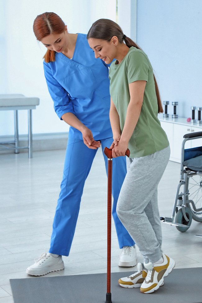 Ärztin unterstützt Rollstuhlfahrerin bei Gehübungen.